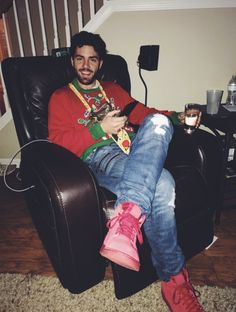 a man sitting in a chair with his legs crossed and holding a cell phone, smiling