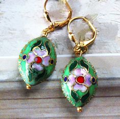 These beautiful earrings feature a hand painted flower in emerald green on a 3D puff oval.  Metal is made of zinc and plated in gold. Hanging from a surgical steel lever-back, it measures 1.5" in length. Earrings are light weight and sway gracefully as you move about your day. Earrings are painted on both side, round disc measures 1 inch.  These delightful dangle earrings are unique, feminine and eye-catching, a great accent to any wardrobe. Available with sculpted clip-on earrings top, please s Elegant Green Enamel Flower Earrings, Green Teardrop Enamel Jewelry, Green Vintage Flower Earrings For Gift, Elegant Hand Painted Green Earrings, Green Vintage Flower Earrings As Gift, Green Drop Flower Earrings, Green Flower-shaped Pierced Earrings, Green Flower Shaped Earrings Gift, Green Flower Drop Earrings