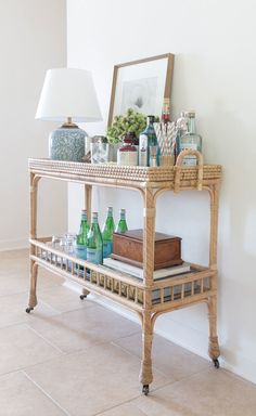 a wicker shelf with bottles and glasses on it in front of a white wall