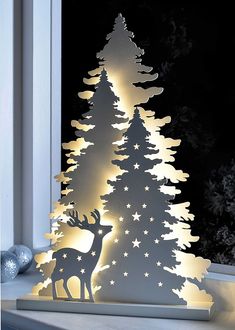 an illuminated christmas tree next to a window with snowflakes on the windowsill