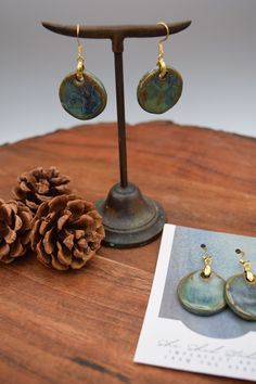 a pair of earrings sitting on top of a wooden table next to a pine cone