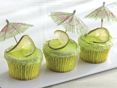 three cupcakes with green frosting and umbrella decorations on top, sitting on a white plate