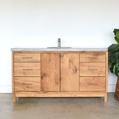 a bathroom vanity with wooden drawers and a marble counter top next to a potted plant