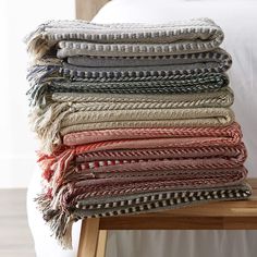 a stack of woven blankets sitting on top of a wooden table next to a bed