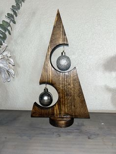 a wooden christmas tree with bells and ornaments on it's sides, sitting in front of a white wall