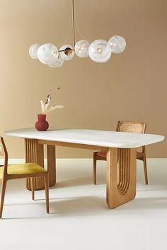 a dining table with four chairs and a vase on it in front of a beige wall