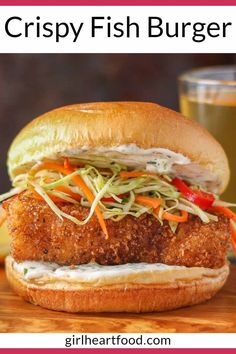 a fried chicken sandwich with cole slaw and carrots on a wooden cutting board