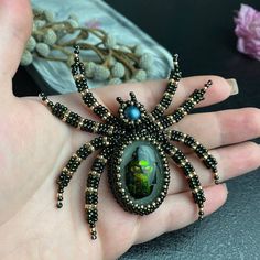 a spider brooch sitting on someone's hand with some beads around it and flowers in the background