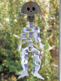 a paper skeleton hanging from a window with trees in the backgroung behind it