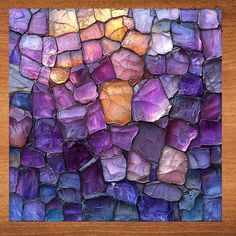 a piece of art made out of rocks on a wooden surface with the colors of purple, yellow and orange