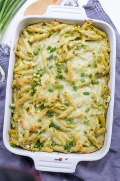 a casserole dish filled with pasta and green onions on a blue towel next to asparagus