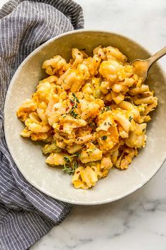 a white bowl filled with macaroni and cheese on top of a marble counter