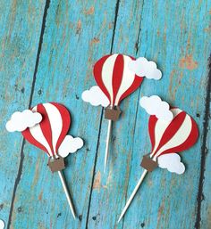 three red and white hot air balloons with clouds on them sitting on a blue wooden surface