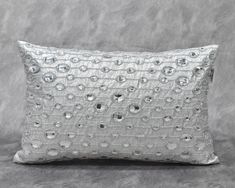 a white pillow with silver sequins on the front and back, sitting on a gray background