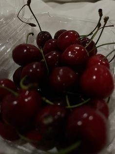 a plastic container filled with lots of cherries on top of a white tablecloth