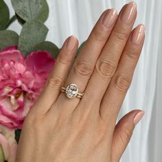 a woman's hand with a ring on it and pink flowers in the background