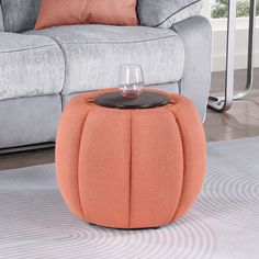 an orange ottoman with a wine glass on it in front of a gray couch and white rug