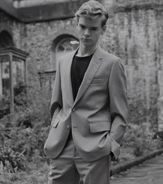 a young man in a suit standing on a brick walkway next to an old building