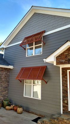 a gray house with red awnings on the front door and windows above it