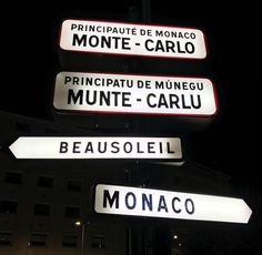 three street signs are lit up in the dark at night, with one pointing to monte - carlo and the other pointing to monte - carlo