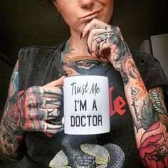 a tattooed woman holding a coffee mug with trust me i'm a doctor written on it