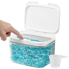 a plastic container filled with lots of blue beads next to a cup on a white surface