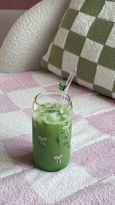 a glass filled with green liquid sitting on top of a pink and white checkered blanket