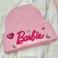 a pink beanie hat with the word barbie written on it and some jewels attached to it