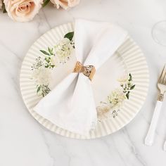 a white plate with flowers on it next to silverware and napkins in front of roses