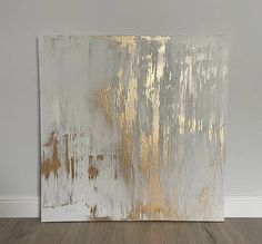 an abstract painting with gold and silver paint on it's side, against a white wall