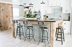 a kitchen island with four stools in front of it and flowers on the counter