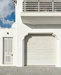 a white building with two garage doors and a balcony on top of it, in front of a cloudy blue sky