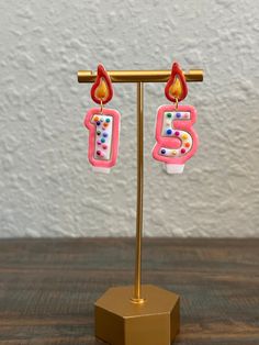 a pair of pink and white earrings on a gold stand with a wall in the background