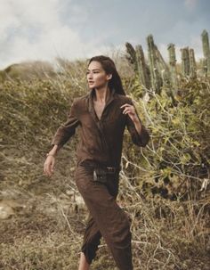 a woman is running through the desert with cactus in the backgrouund and her hand on her hip