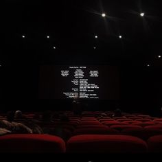 an empty theater with rows of red seats in front of a screen that reads,