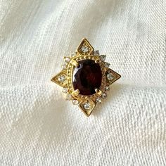 a gold ring with a large red stone surrounded by small white and clear stones on a white cloth