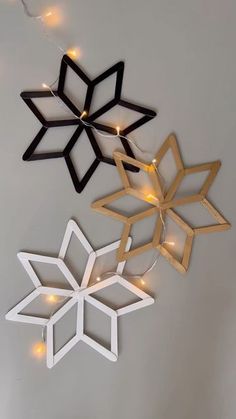 three paper snowflakes are hanging on the wall with fairy lights around them,