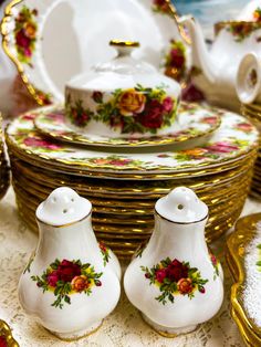 there are many dishes and cups on the table with gold rimmed plates in the background