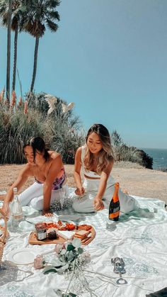 two women sitting on the beach with food and drinks