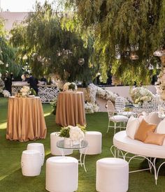 an outdoor wedding setup with white chairs and tables covered in gold cloths, surrounded by lush greenery