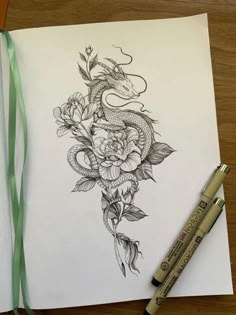 a pencil drawing of a dragon and flowers on paper with green ribbon next to it