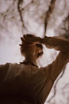 a man standing in front of trees with his hands on his head and looking up at the sky