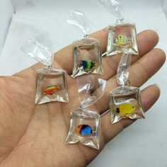 five small fish in clear bags sitting on someone's hand with their fingers together