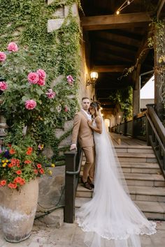 a bride and groom posing for a photo in front of some flowers on the stairs