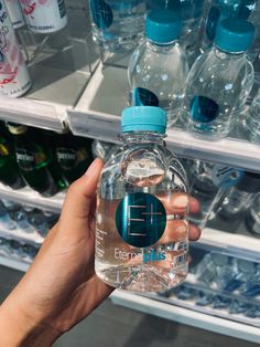 a person holding up a bottle of water in front of a shelf of bottled water