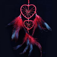 a red heart shaped dream catcher hanging from a string on a black background with feathers