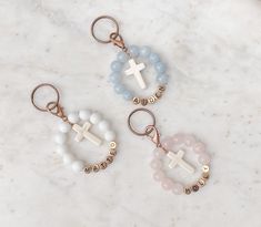 three keychains with cross charms on them sitting on a marble counter top,