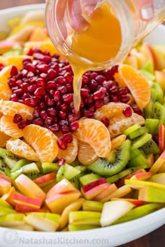 someone is pouring orange juice into a bowl of fruit for a healthy salad that includes apples, kiwis and pomegranate