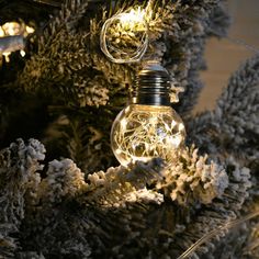 a light bulb is hanging from a tree with snow on the branches and lights around it