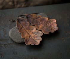 two leaf shaped earrings sitting on top of a rock next to a stone and metal object